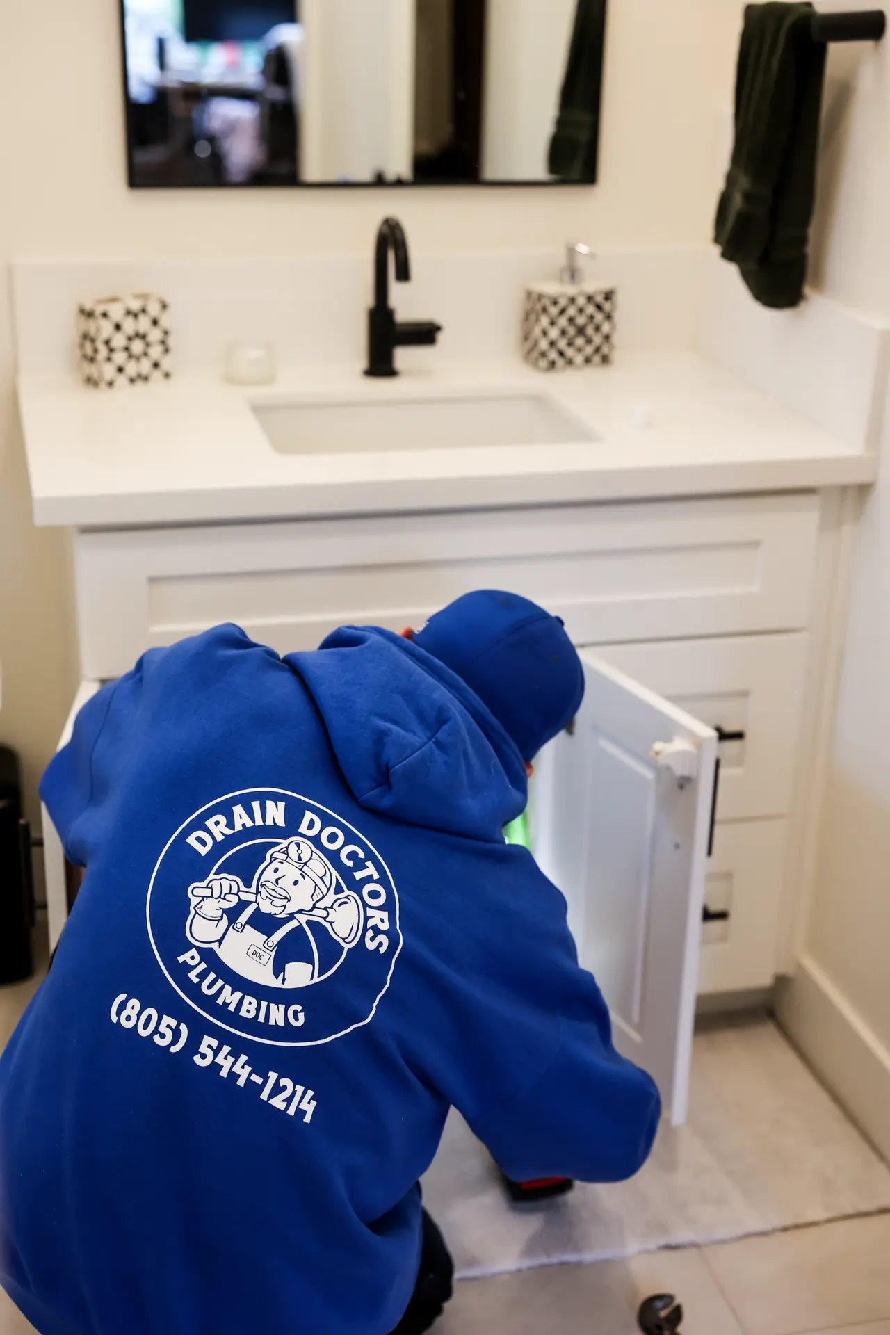 Drain Doctors Plumbing technician checking the pipes inside an open bathroom vanity cabinet