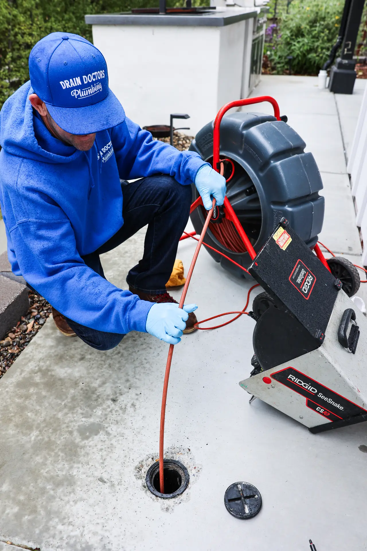 Drain Doctors Plumbing technician feeding a sewer inspection camera into an outdoor cleanout