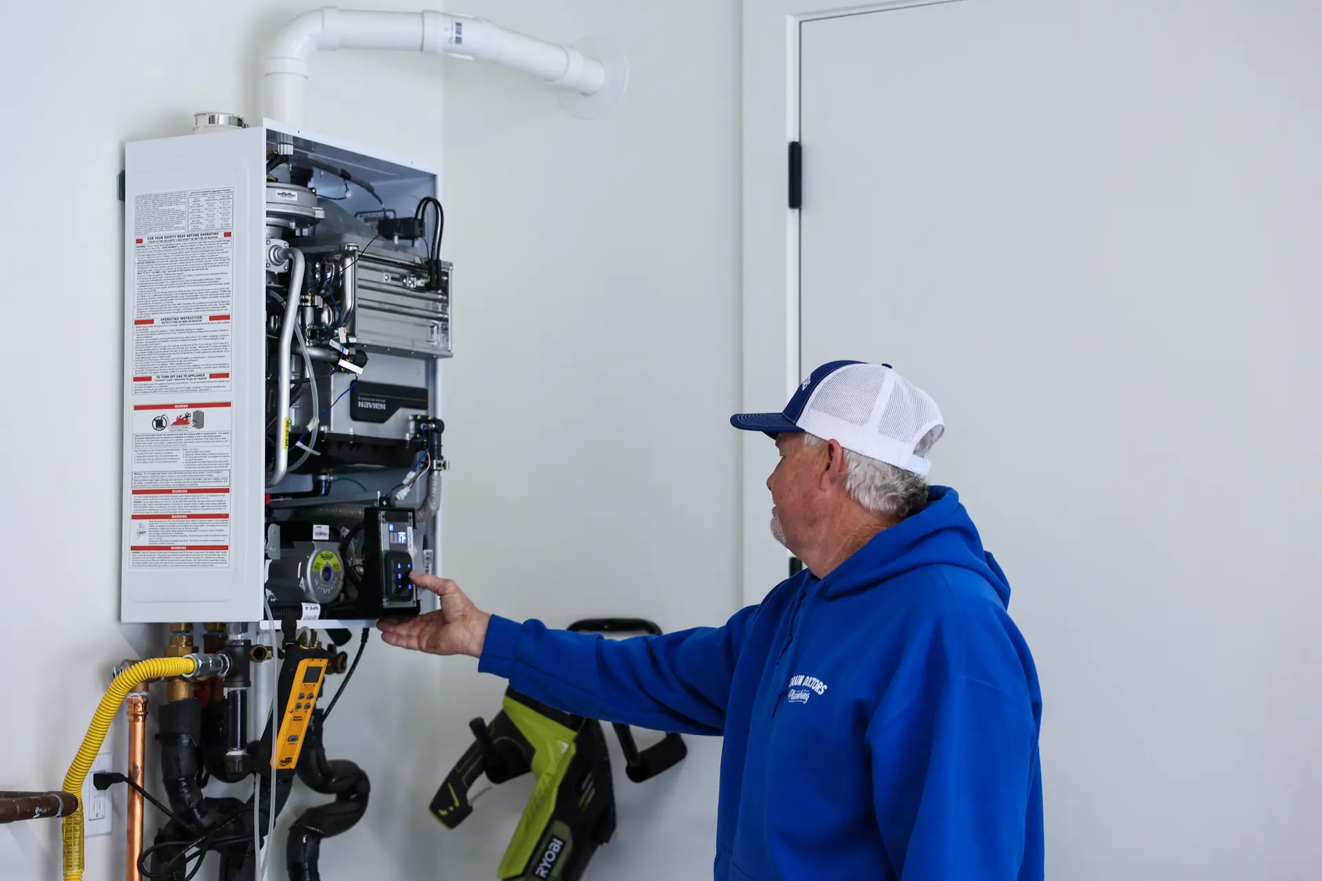 Drain Doctors Plumbing technician checking an open tankless water heater with copper and gas supply lines connected underneath