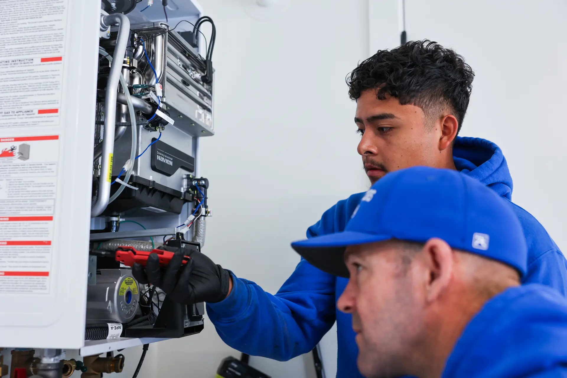 Two Drain Doctors Plumbing technicians working inside an open wall-mounted tankless water heater