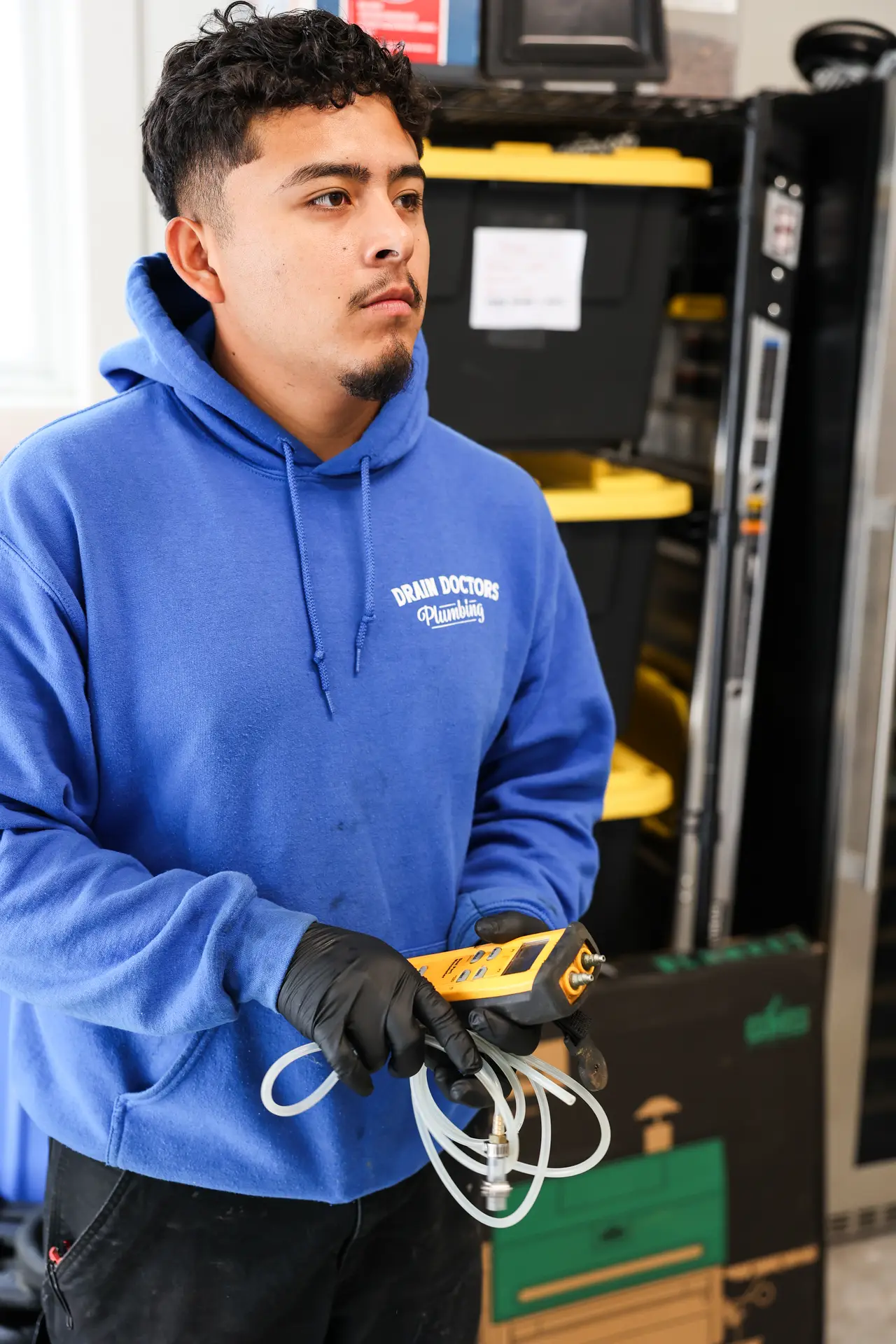 Drain Doctors Plumbing technician holding a gas pressure tester with test hoses in the shop