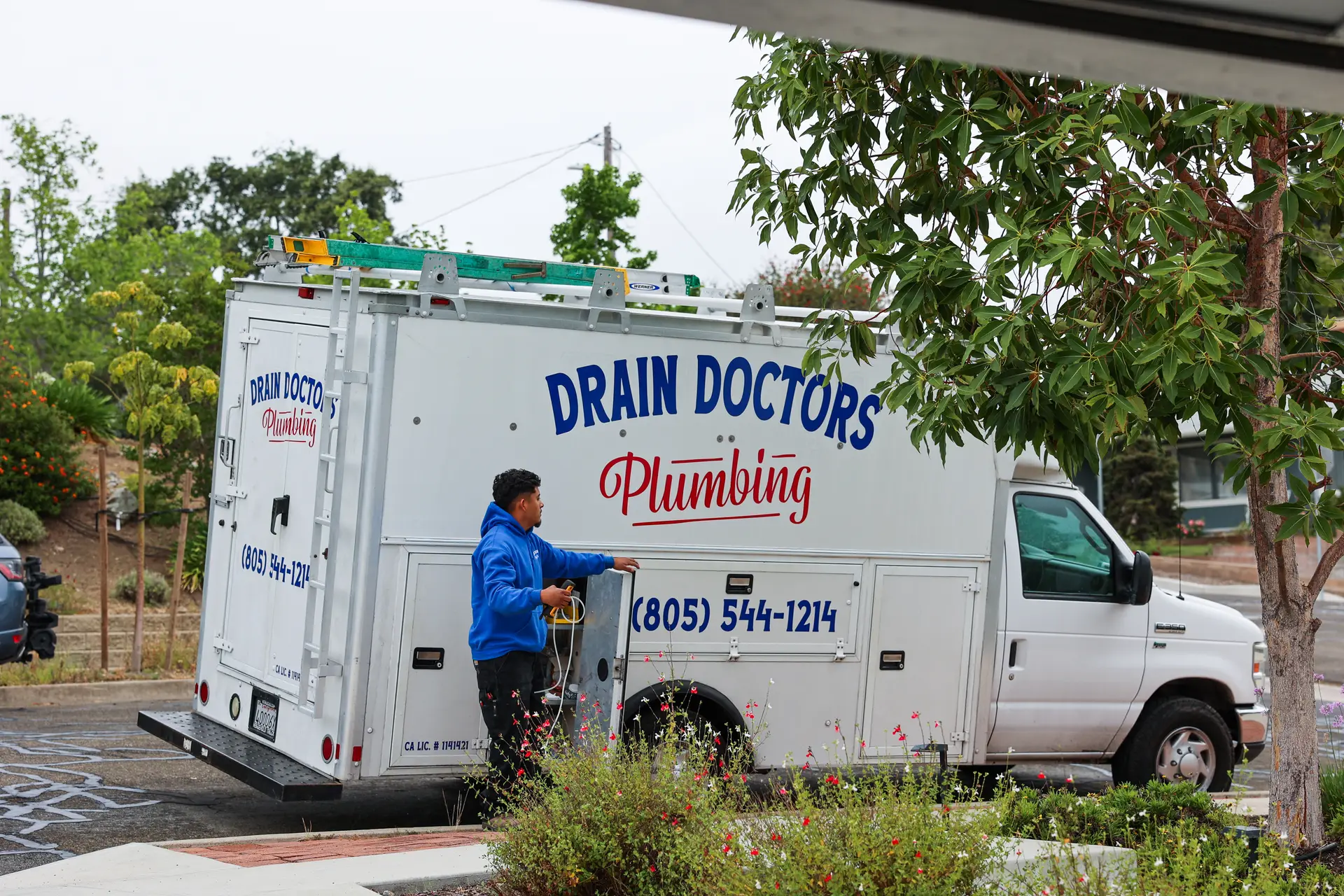 Drain Doctors Plumbing technician pulling equipment from a side compartment of the service truck