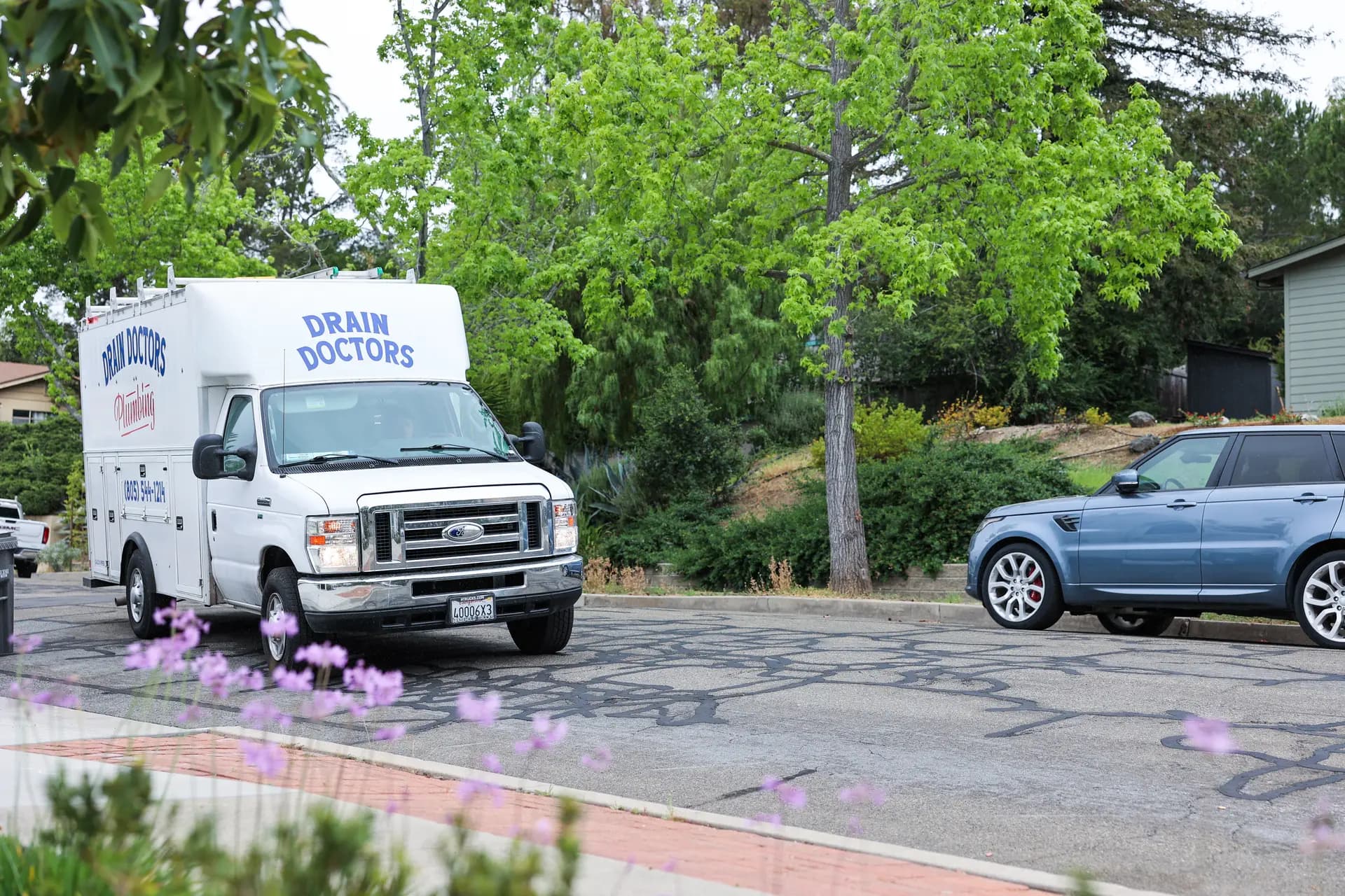 Drain Doctors Plumbing service truck driving down a tree-lined residential street