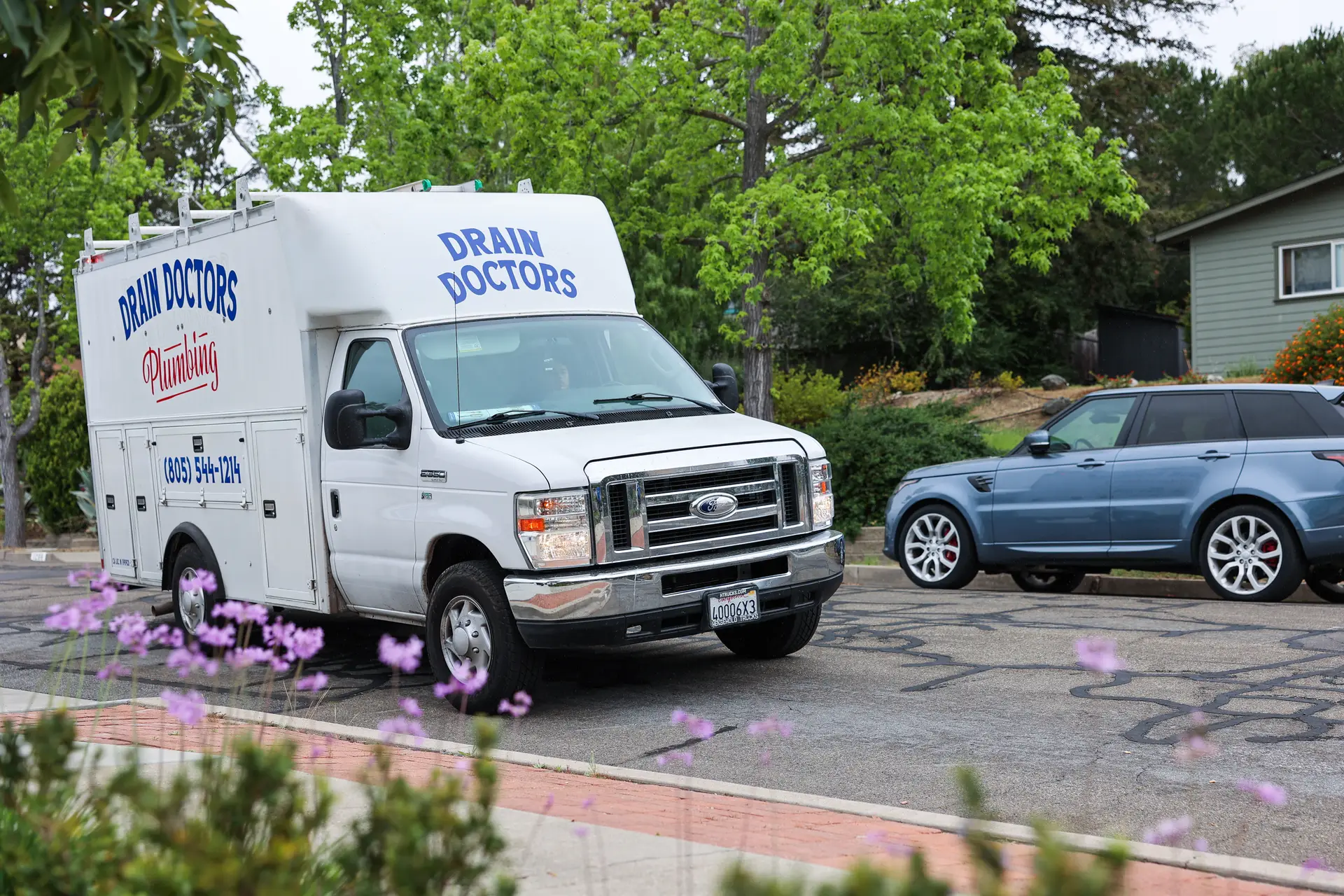 Drain Doctors Plumbing service truck pulling up to a home with a landscaped front yard