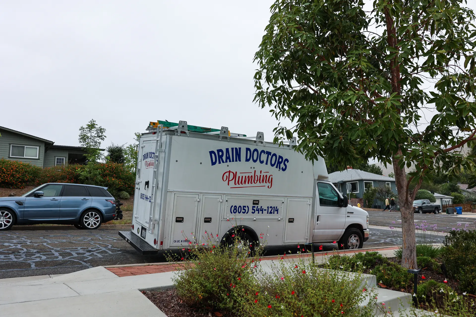 Drain Doctors Plumbing service truck parked at the curb on a residential street lined with older homes