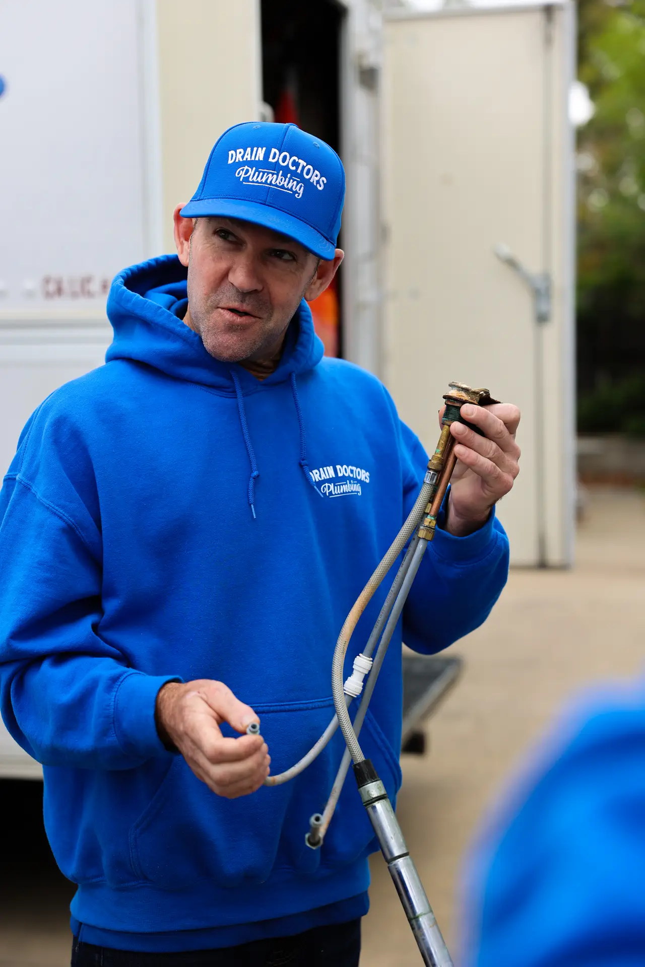 Drain Doctors Plumbing technician holding an old faucet with its supply lines outside a work truck