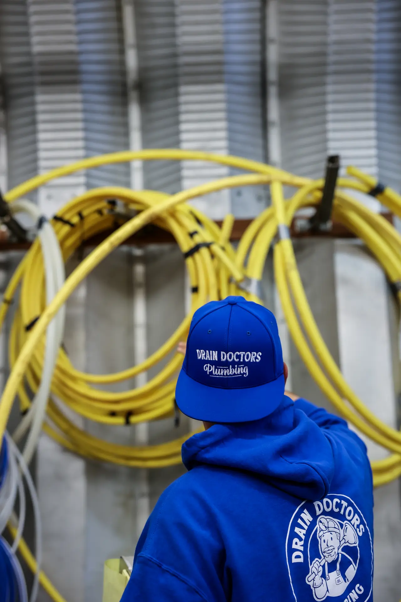 Drain Doctors Plumbing technician reaching for yellow gas line coiled on a shop wall rack