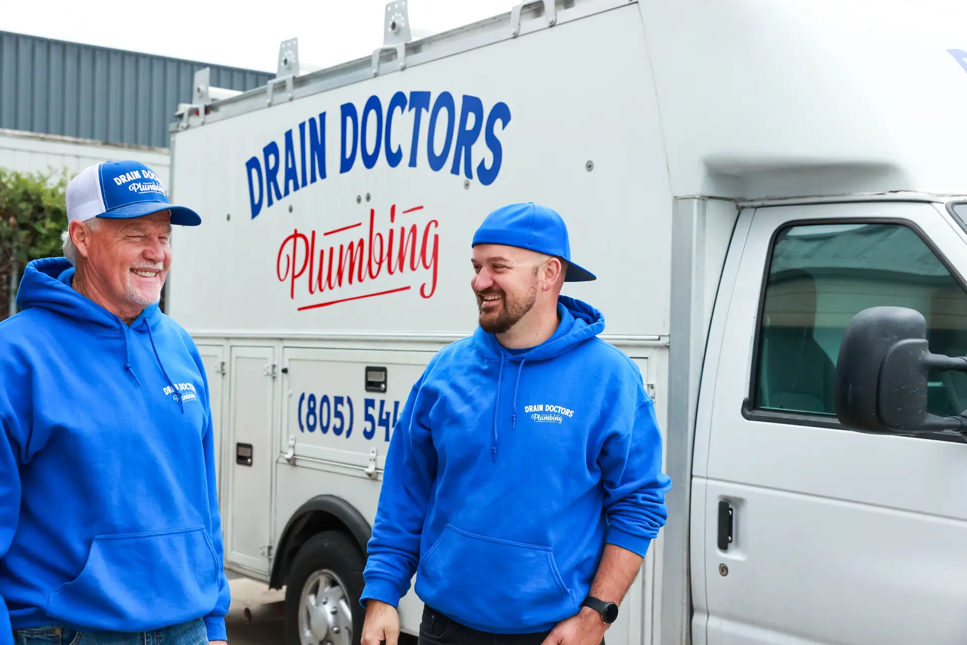 Two Drain Doctors Plumbing technicians in blue hoodies talking beside the company service truck
